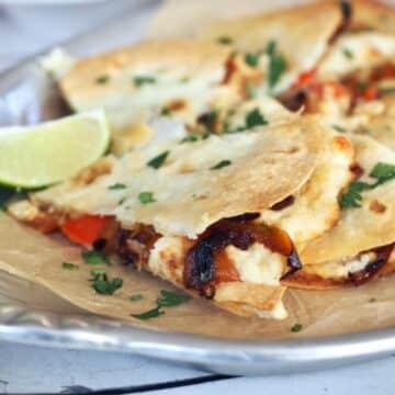 Crispy chicken and cheese quesadilla with grilled peppers and onions on a platter.