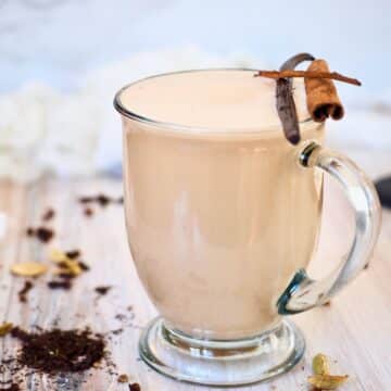 Chai tea latte in glass mug garnished with cinnamon stick and vanilla bean.