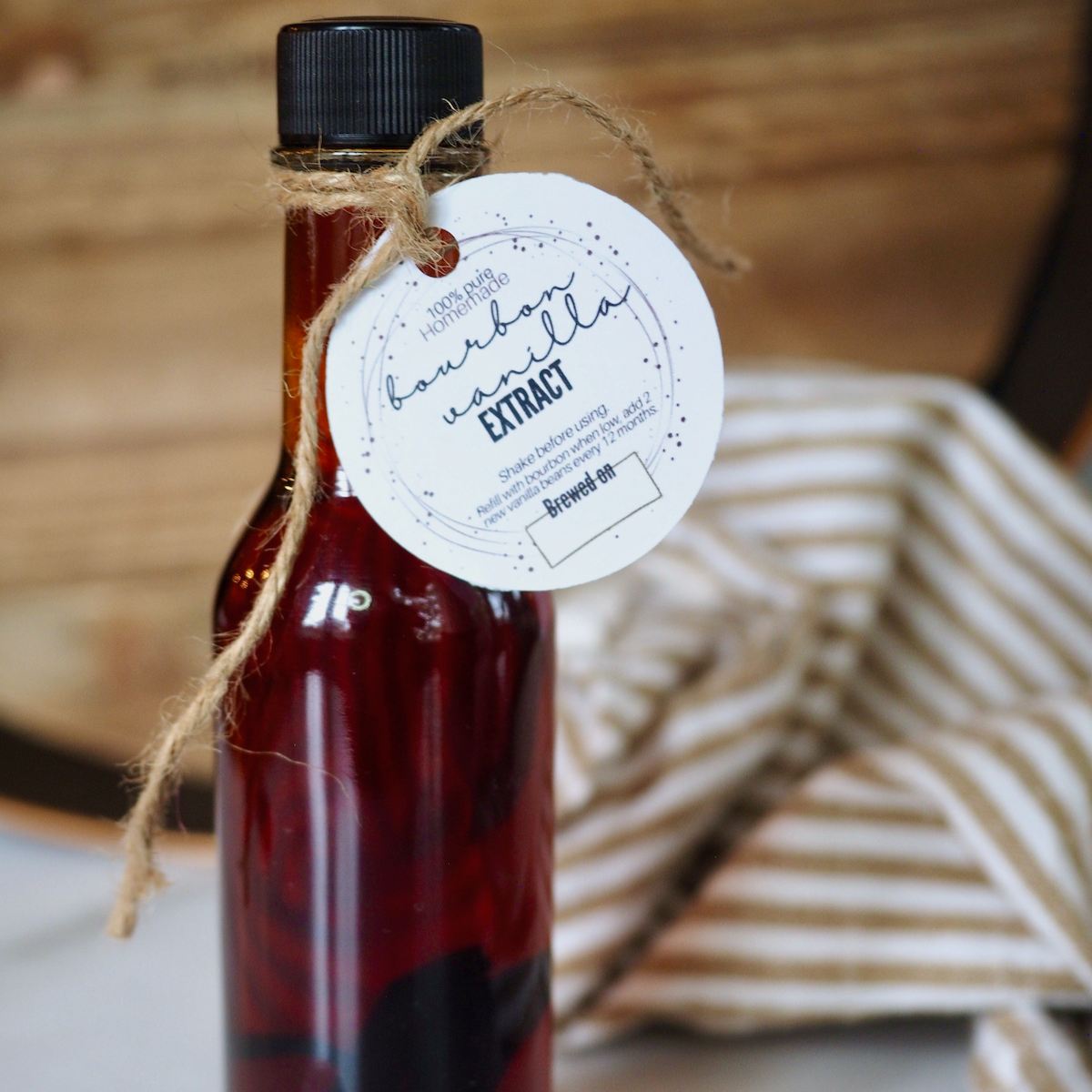 A small glass bottle filled with dark bourbon vanilla extract tied with a printable label. 