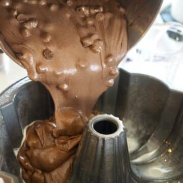 Pouring chocolate chocolate chip batter into prepared bundt pan.