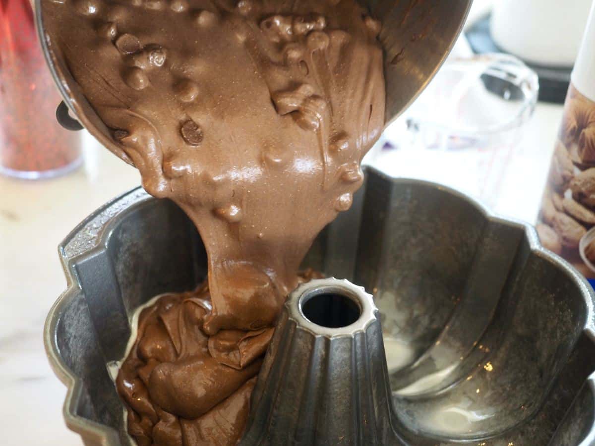 Pouring chocolate chocolate chip batter into prepared bundt pan.