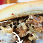 Pin for best shaved steak sandwich cheesesteak sandwich with image of close up of shaved steak cooked with sauce and melted cheese on a roll.
