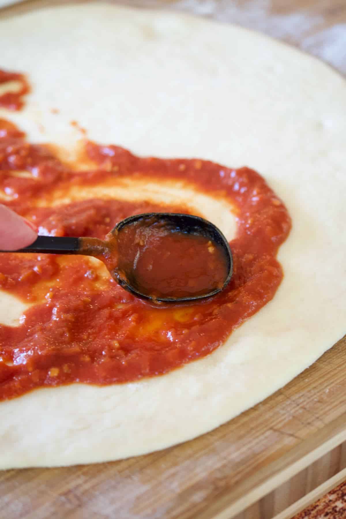 Spooning homemade pizza sauce on no rise pizza dough.