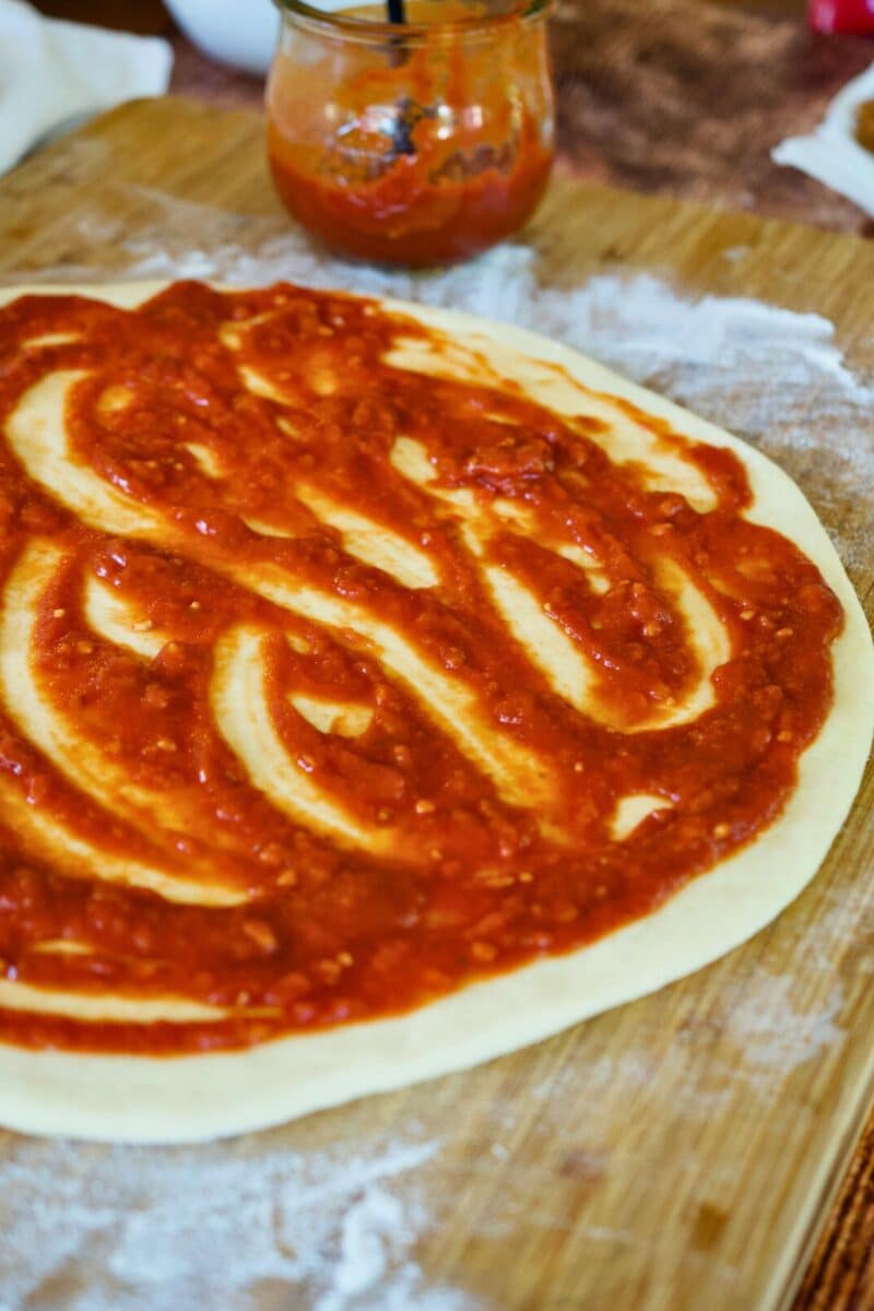 Pizza dough on floured board spread with pizza sauce. 