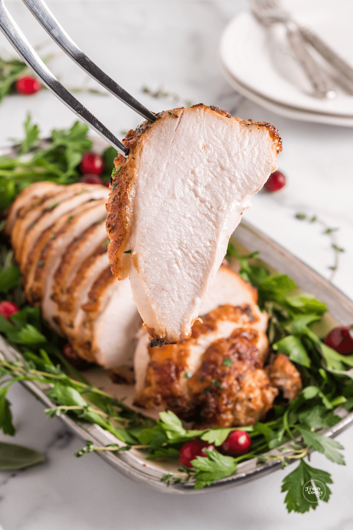 A beautiful turkey breast on a platter, with a meat fork on a slice. 