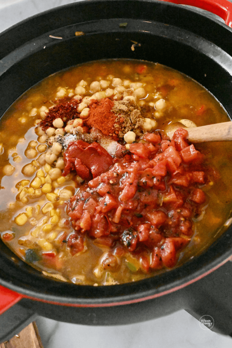 https://www.thefreshcooky.com/wp-content/uploads/2023/01/stirring-in-tomatoes-corn-garbanzos-to-soup-800x1200.png