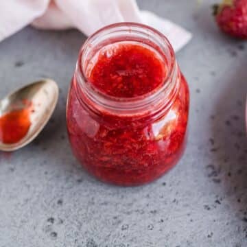 A jar of low-sugar strawberry freezer jam on the counter with a spoon.