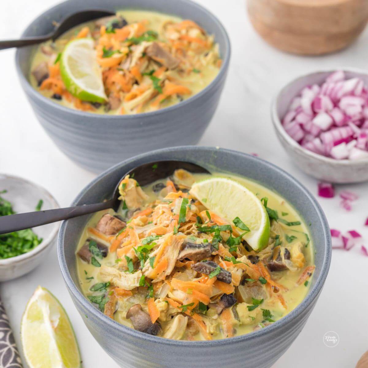 Thai coconut chicken soup in bowls, topped with a wedge of lime and cilantro.