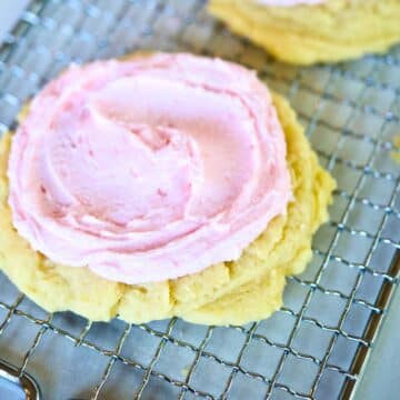 A large copycat Crumbl Sugar cookie frosted with pink almond icing on a wire rack.