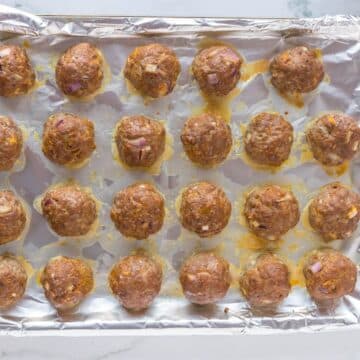 Cooked meatballs lay in neat rows on a pan lined with aluminum foil.