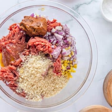 Raw ground beef, red onion, ginger, seasonings, egg and panko sit in a bowl together.