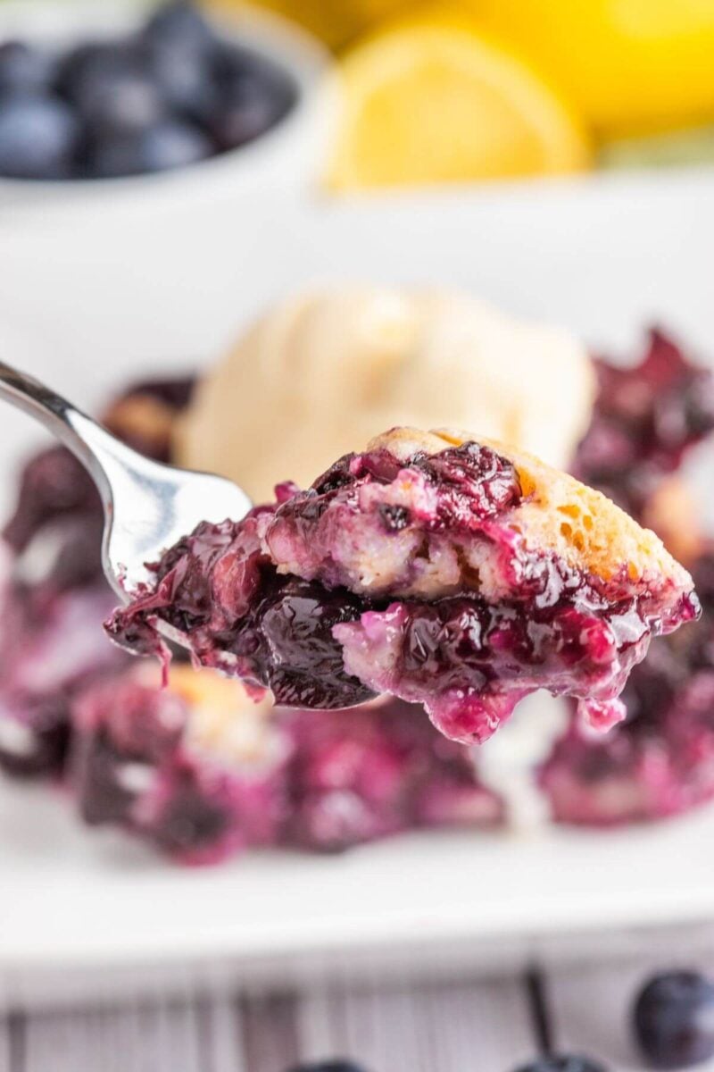 A fork lifts up some baked blueberry dessert above the plate served.