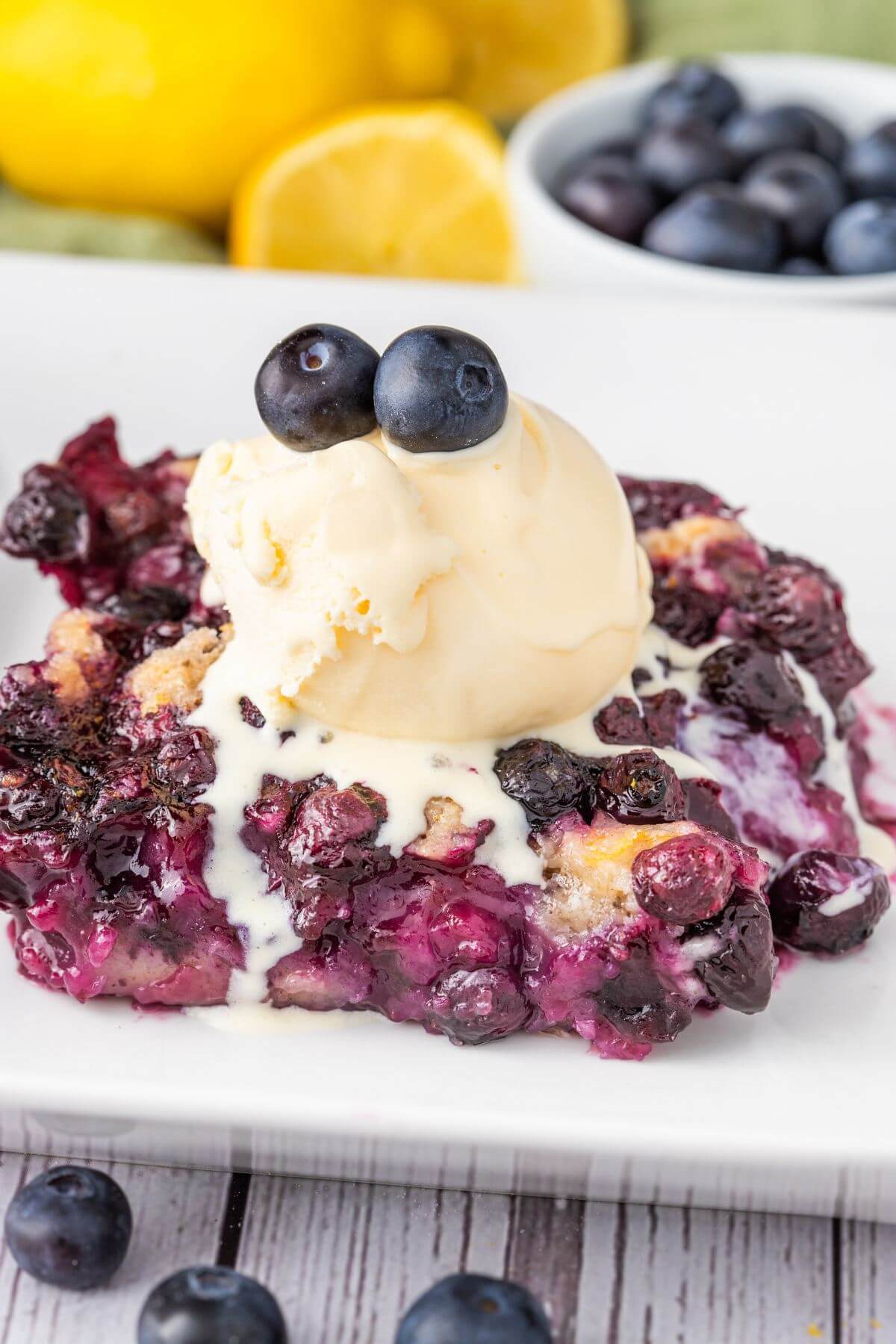 Blueberries baked in a cobbler are covered in melty ice cream.