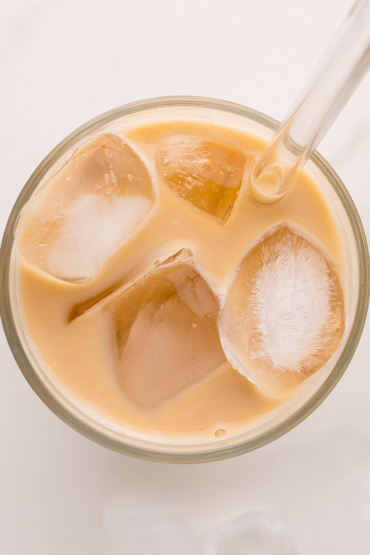 The top of a glass with the straw pointed to the top right corner shows creamy chai drink and ice.