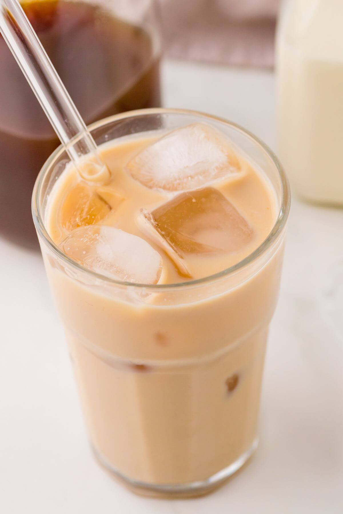 The top and side of a glass with a straw is filled with light brown chai and milk beverage.