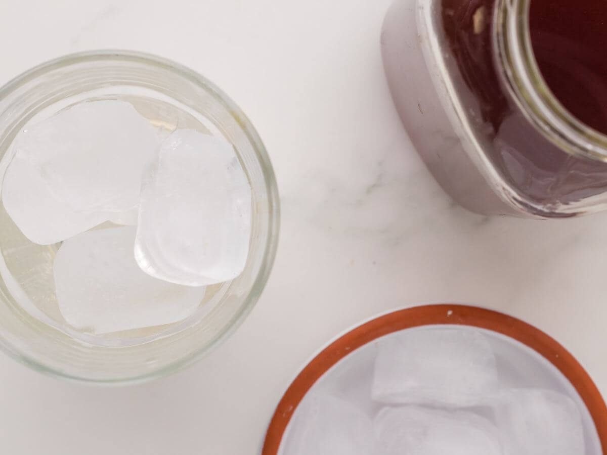 A cup of ice sits next to a jar of dark brown chai tea concentrate.
