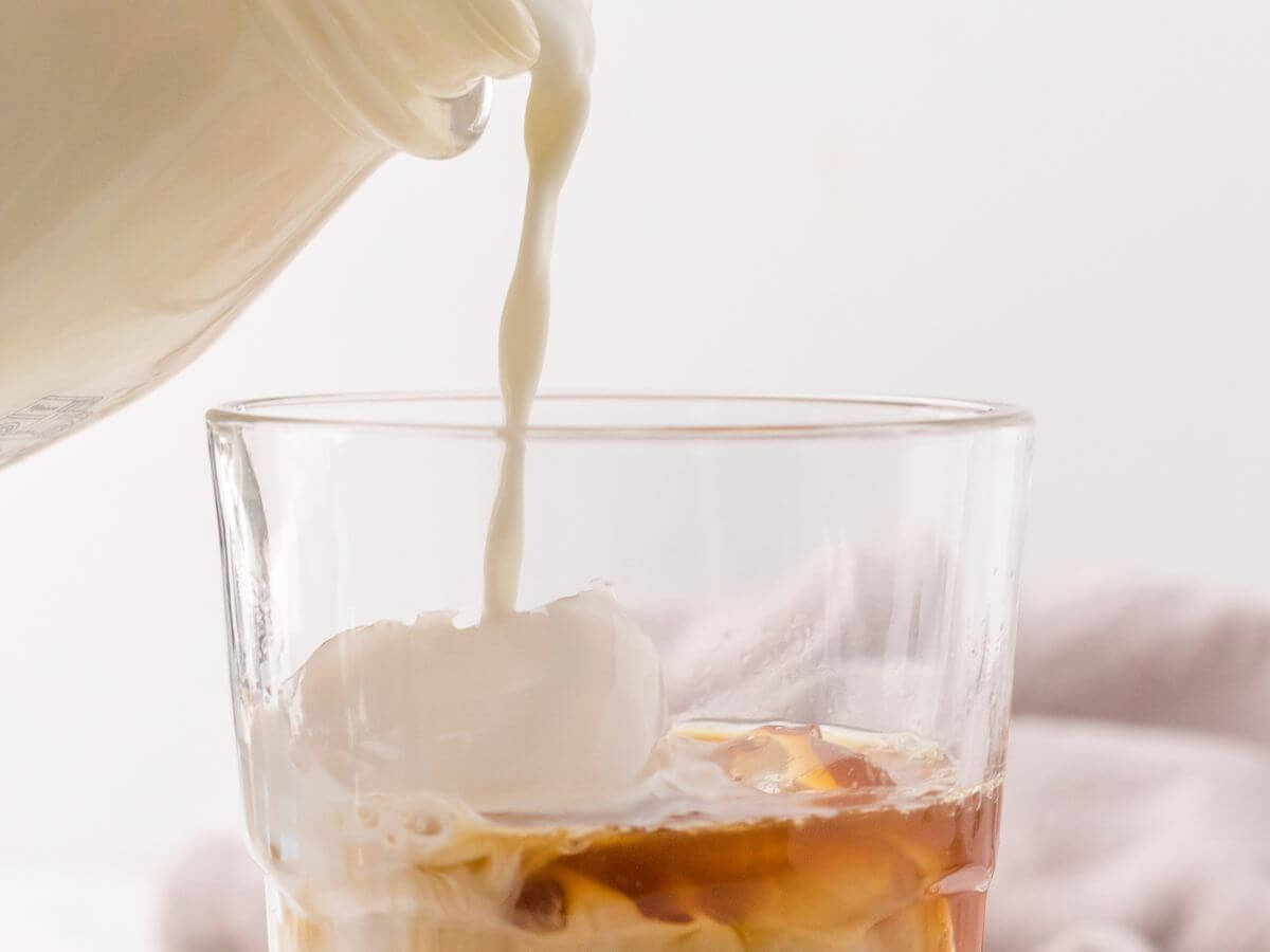 A bottle of milk pours into a glass filled with ice and chai concentrate.