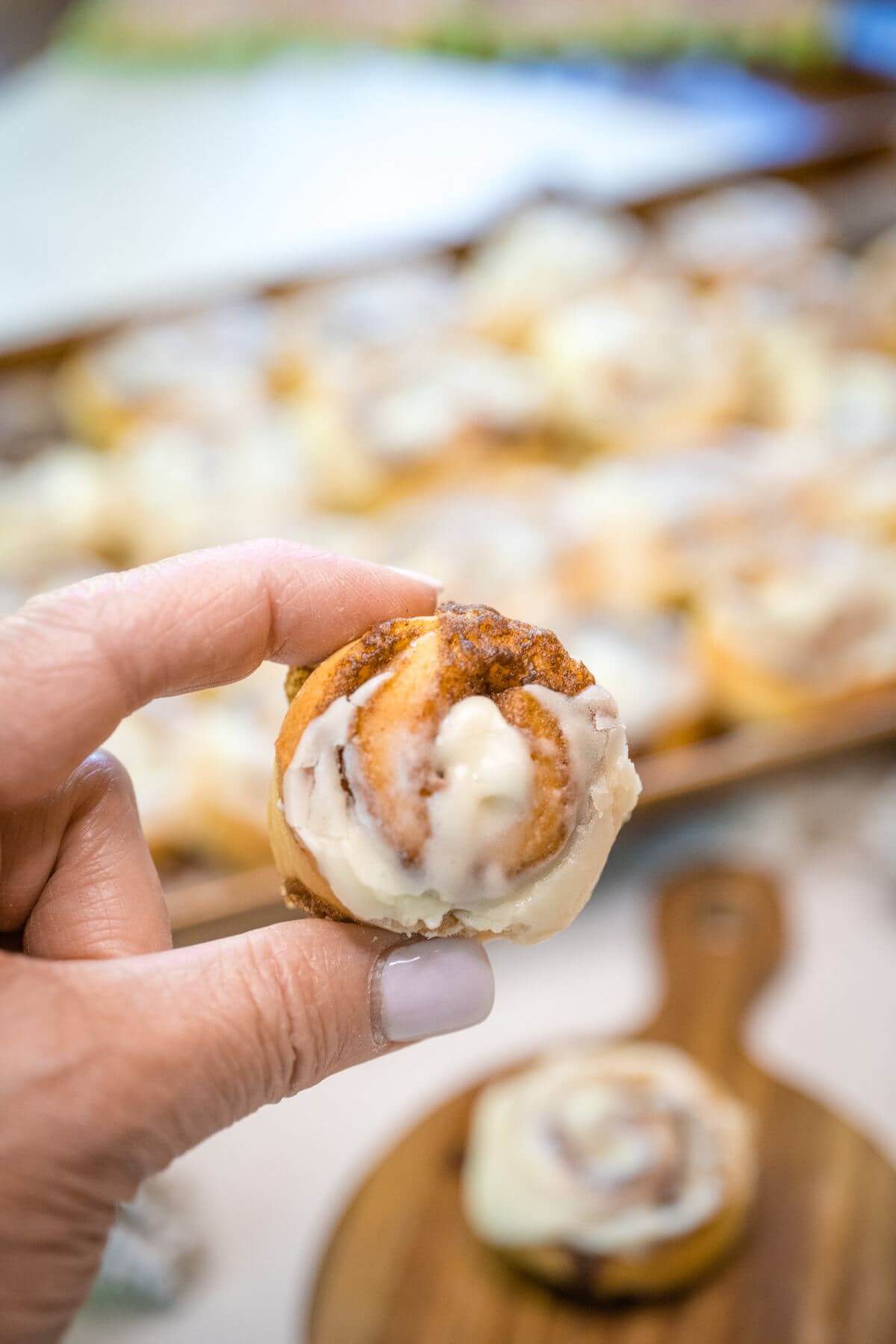 A tiny cinnamon bun is held up by someone's hand high above the pan.