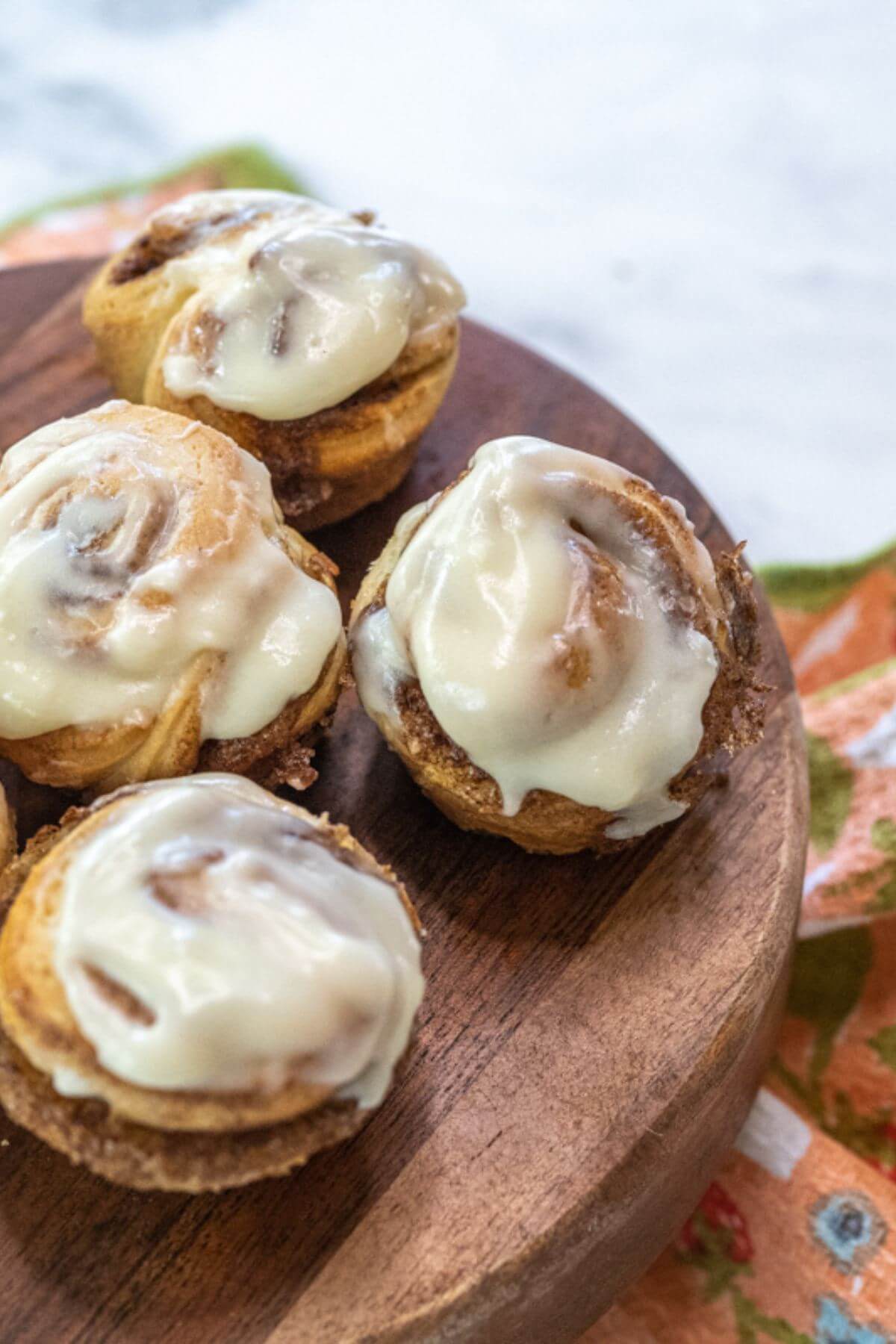 A wooden board holds four iced and glossy tiny cinnamon rolls.
