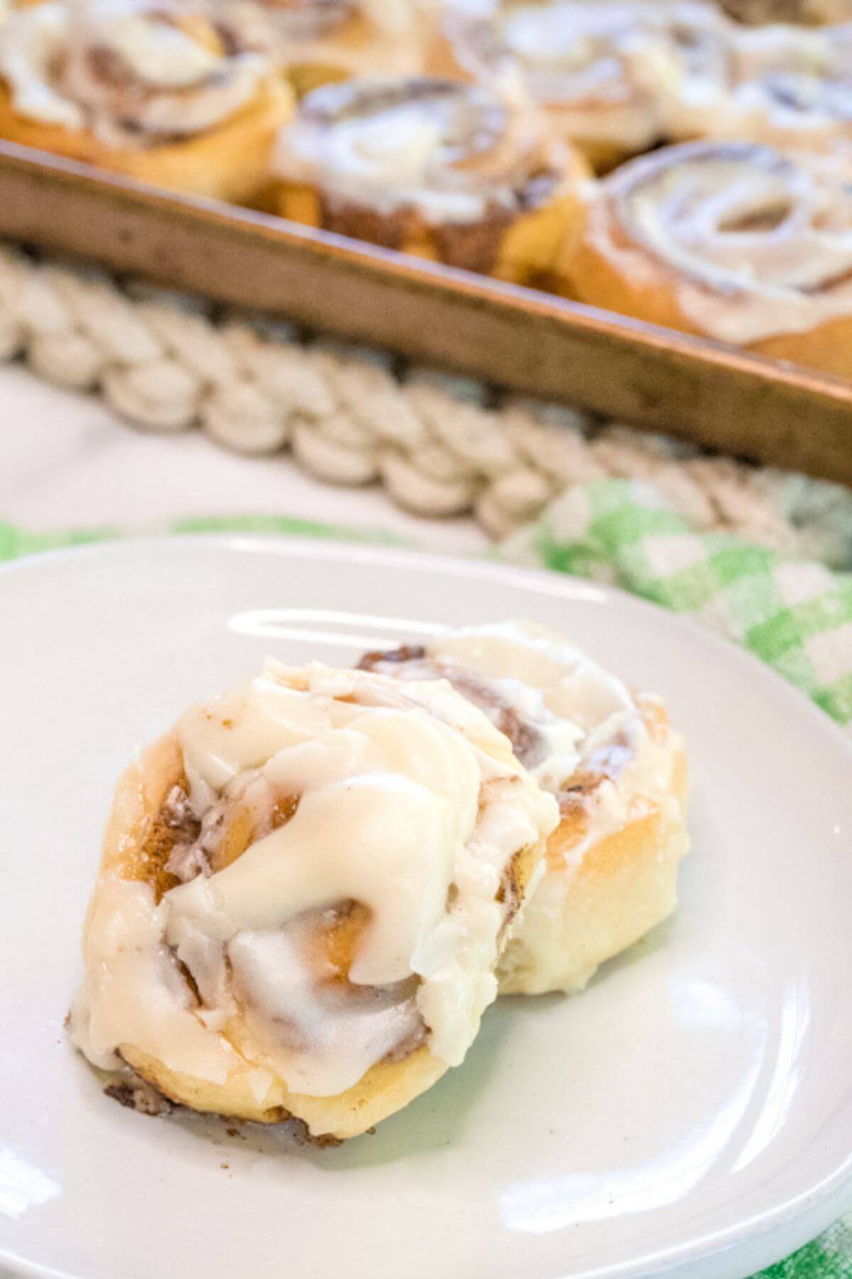 Two cinnamon buns sit overlapping each other on a white saucer near the full pan.