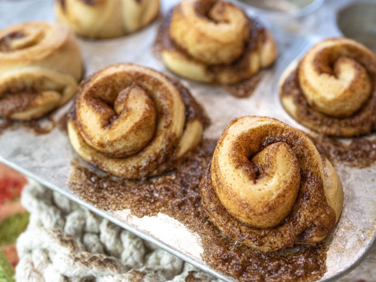 Baked cinnamon rolls are overflowing the muffin tins.