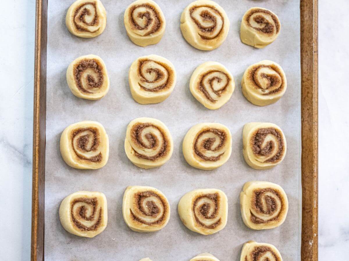 Unbaked cinnamon rolls sit on a parchment lined pan.