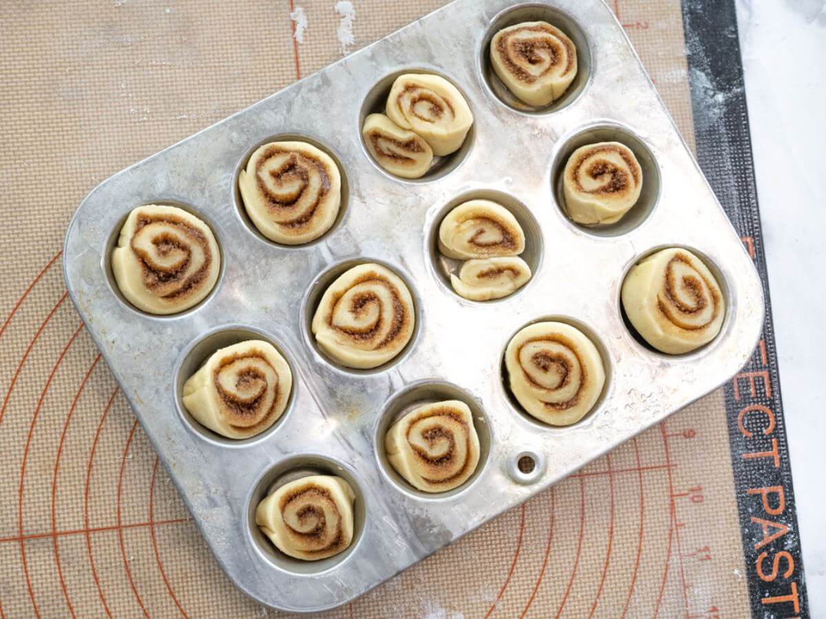 Small unbaked cinnamon rolls sit in muffin tin ready to rise.