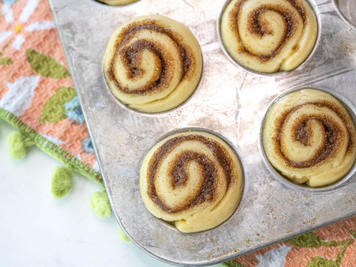 Rolls with cinnamon swirls are in a muffin pan and are starting to puff up.
