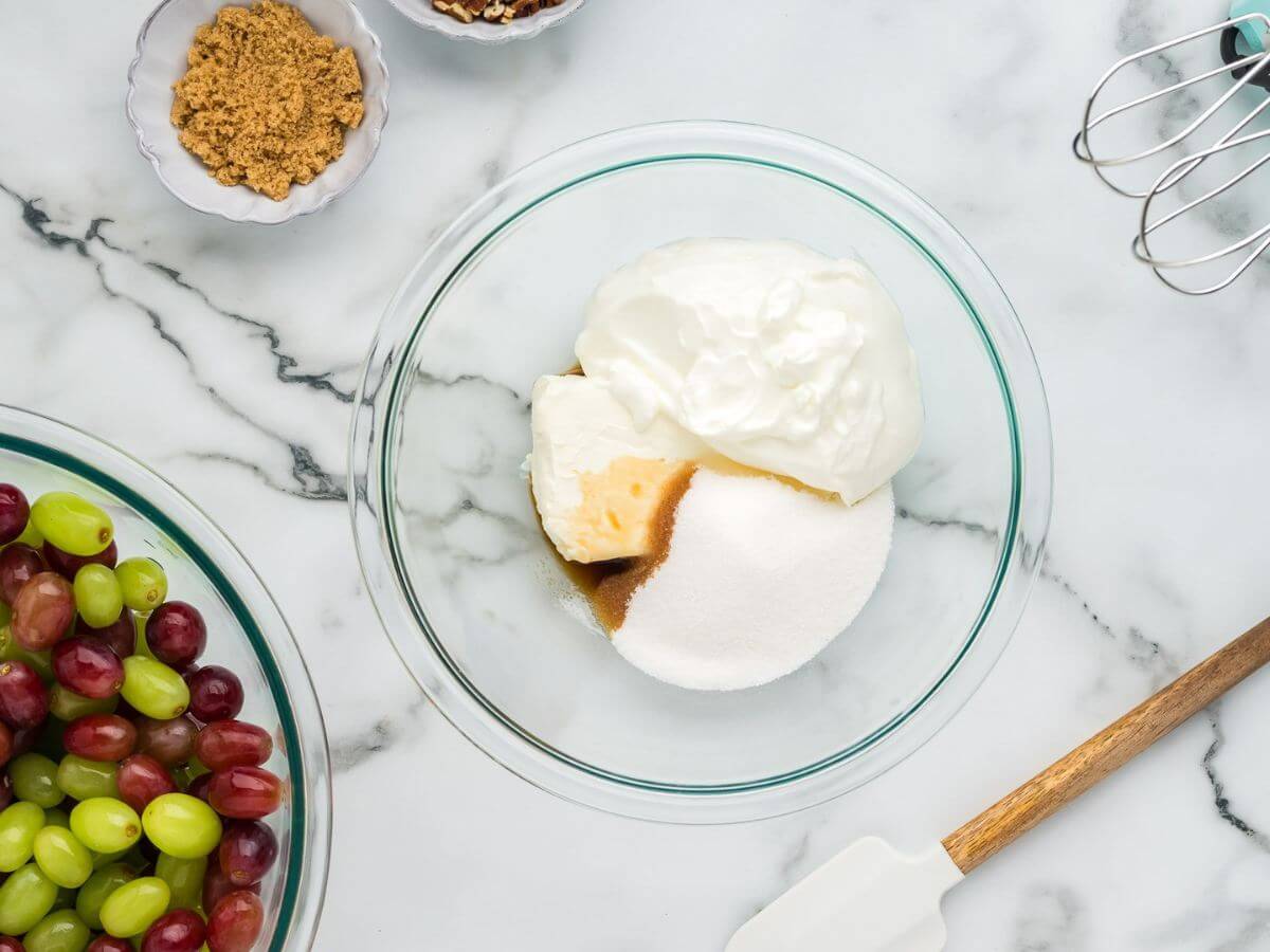 A glass mixing bowl holds cream cheese, sour cream, and sugars.