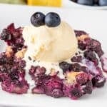 Old fashioned blueberry cobbler serving on a plate with a scoop of vanilla ice cream melting on top.