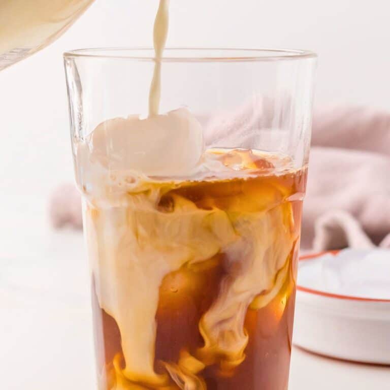 Iced Chai tea latte being made by pouring milk over ice and chai concentrate.