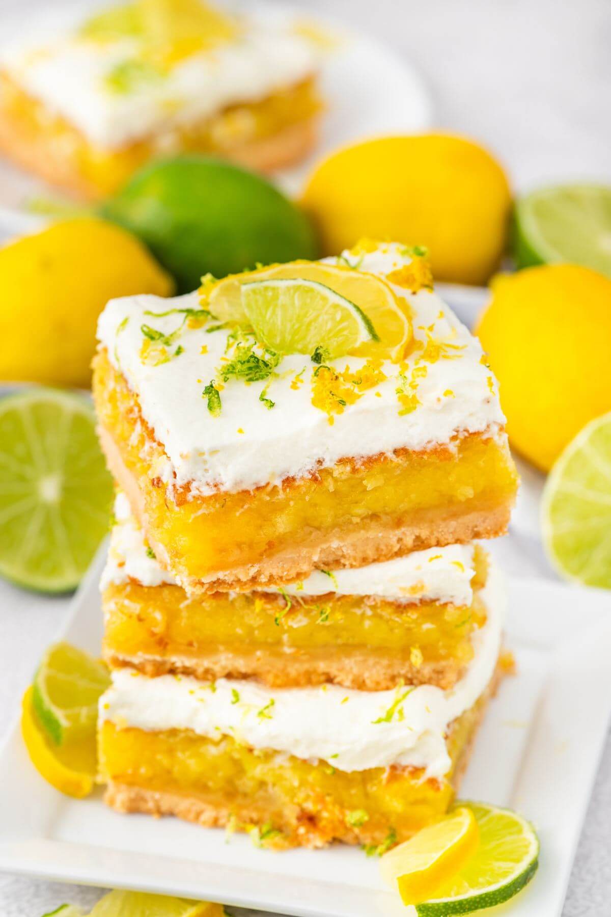 Three yellow dessert squares are stacked on top of each other in front of fresh lemons and limes.