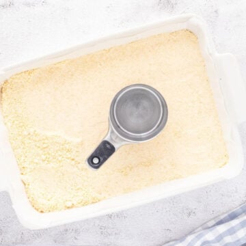 A dry crust layer fills a rectangular baking pan with a measuring cup on top.