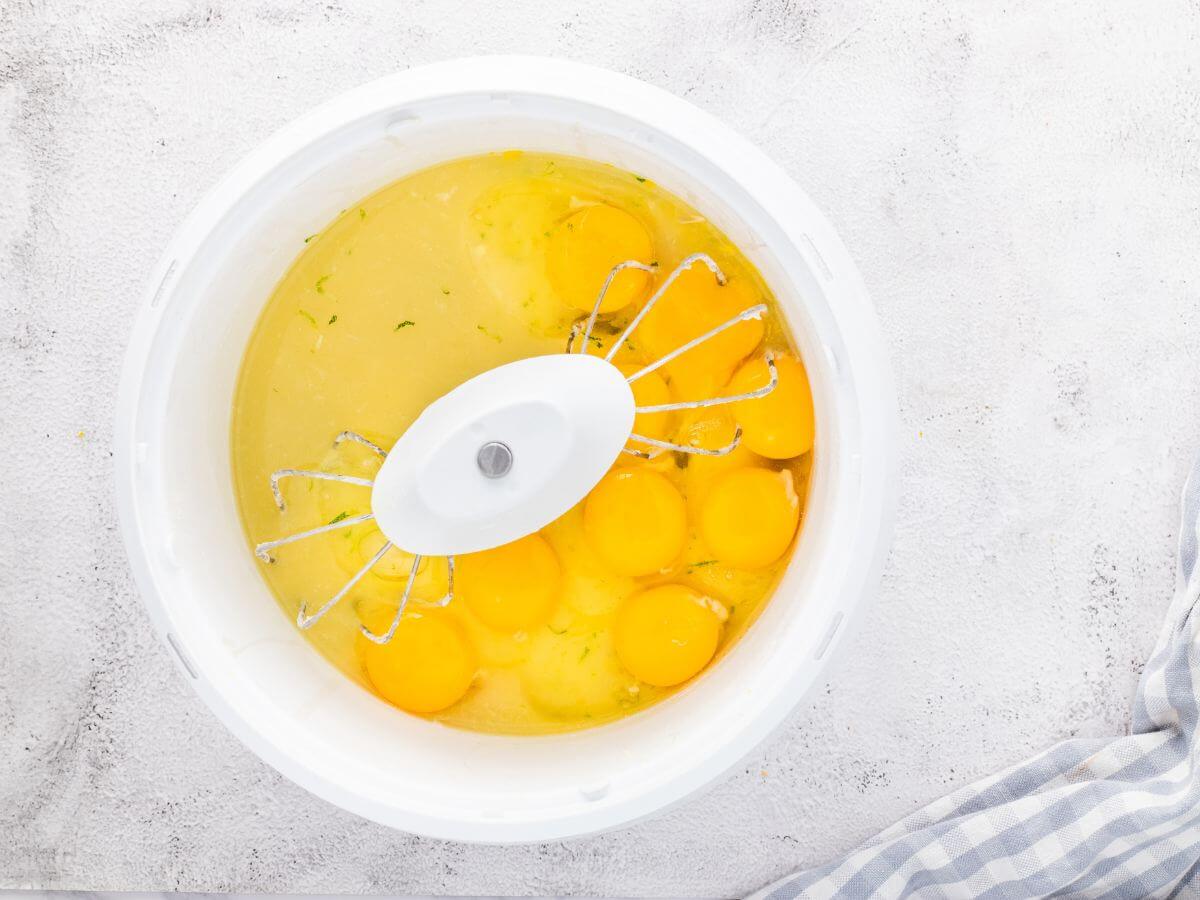 A mixing bowl with mixers stirs eggs and the juice from the fruit into a sugar mixture.