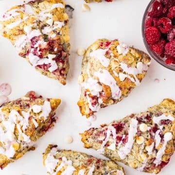 White chocolate raspberry scones drizzled with vanilla glaze and fresh raspberries in a bowl.