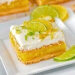 Single square of lemon lime bars on a square plate topped with slices of lemon and limes.