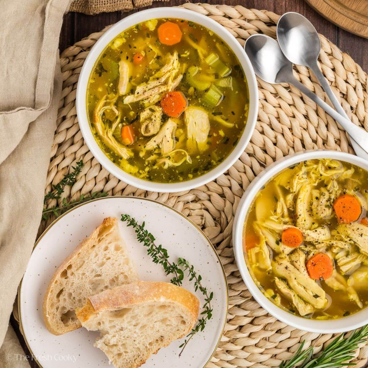 Overhead shot of two bowls of chicken soup served next to a plate of bread.