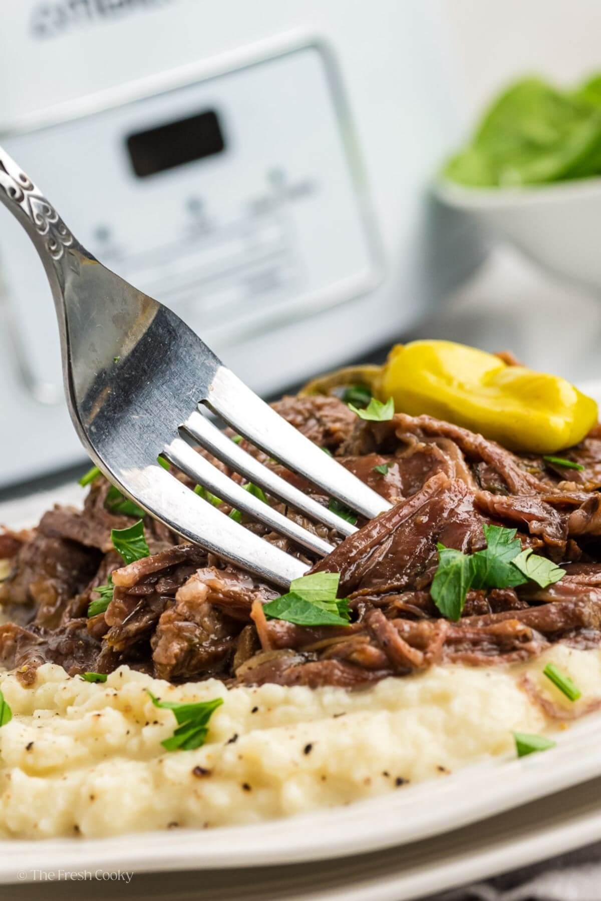 Fork getting a bite of shredded beef with mashed potatoes from a plate.